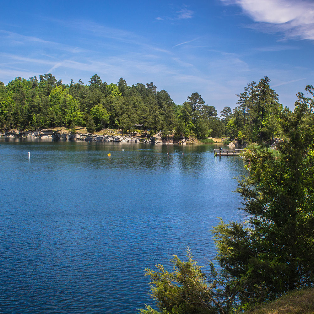 Small body of water surrounded by small cliffs and green spaces with a crystal clear sky in Wake County