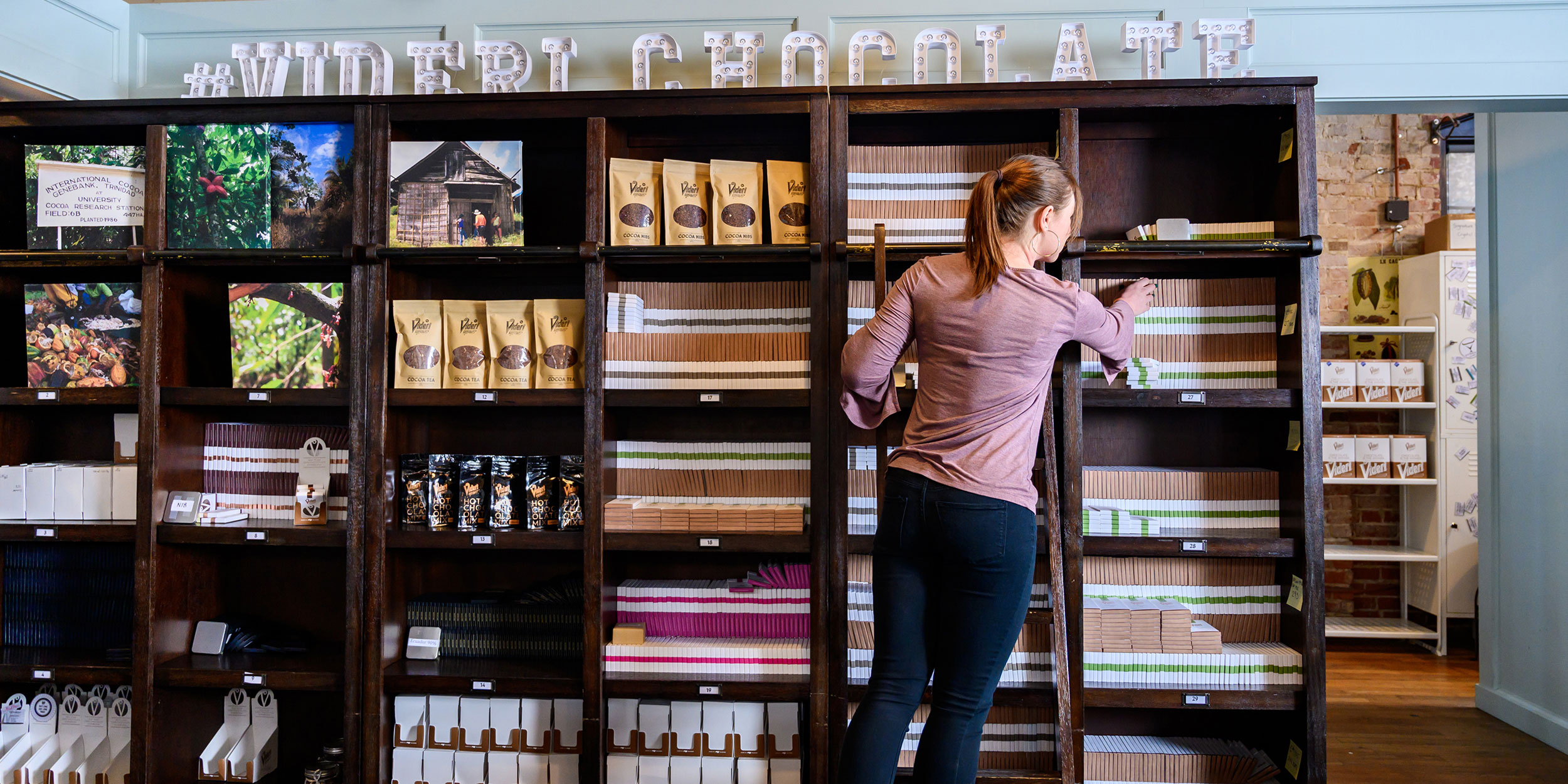 A woman on a ladder organizing and stocking shelves inside a chocolate store in Wake County