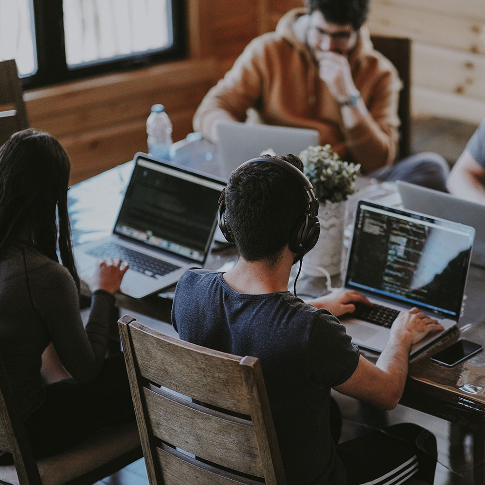 A group of tech workers sit around a table and work on laptops together