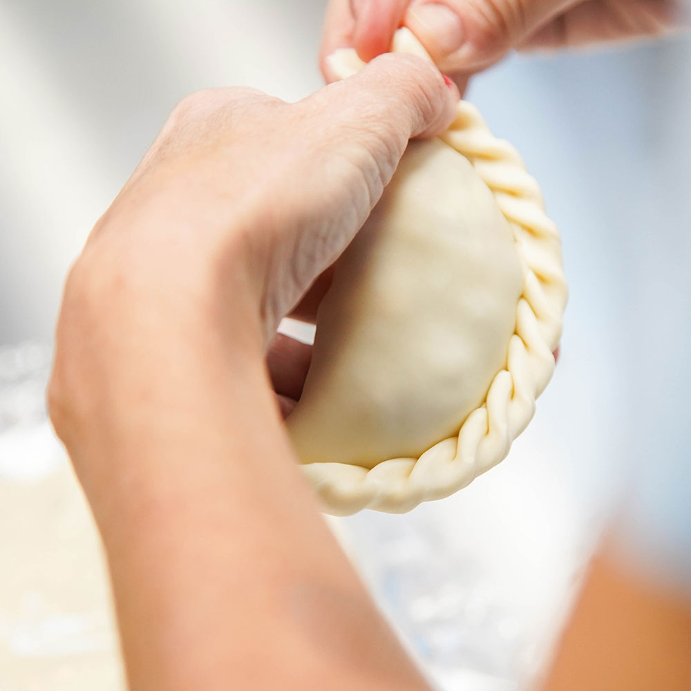 An employee is folding a piece of pastry into a semi circle and pinching the ends of the dough in Wake County