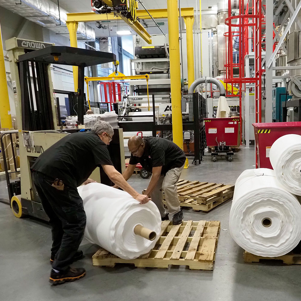 Two men roll large sheets of fabric onto wooden pallets in a warehouse in Wake County, NC