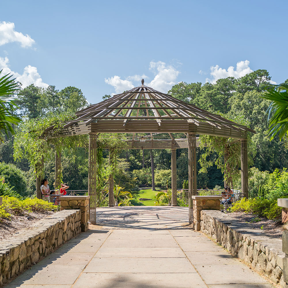 A wooden gazebo surrounded by fanning plants and stone walls with a forest in the near distance located on Duke University in Wake County