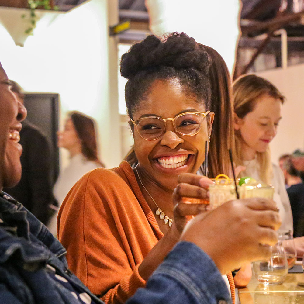 Two women are smiling and toasting drinks to one another in an indoor restaurant in Wake County