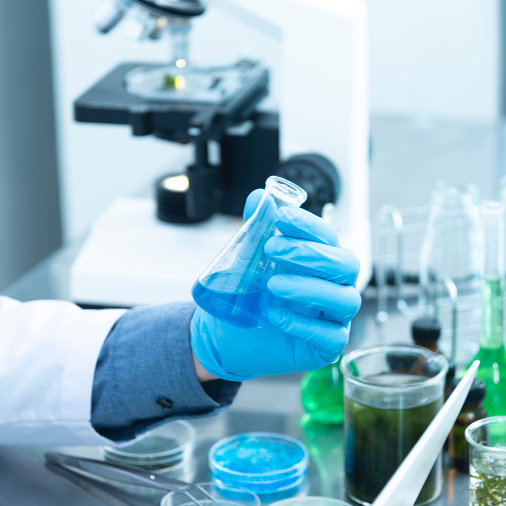 A scientists in a lab wearing latex gloves holds a beaker full of blue liquid