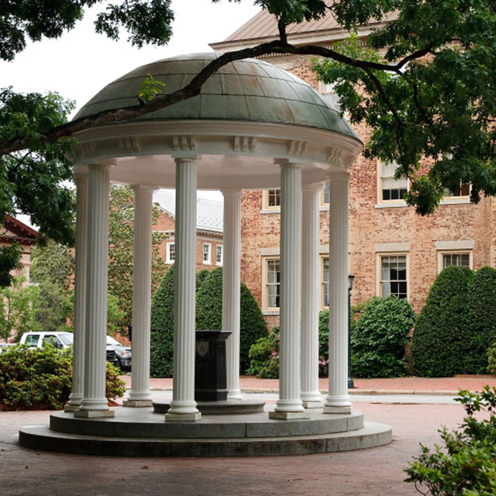 An old well with a white, domed pergola in front of a historic red and white brick building in Chapel Hill in Wake County