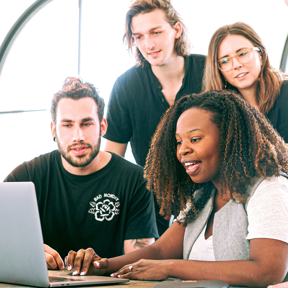 A group of coworkers gather around a laptop to work on a project together