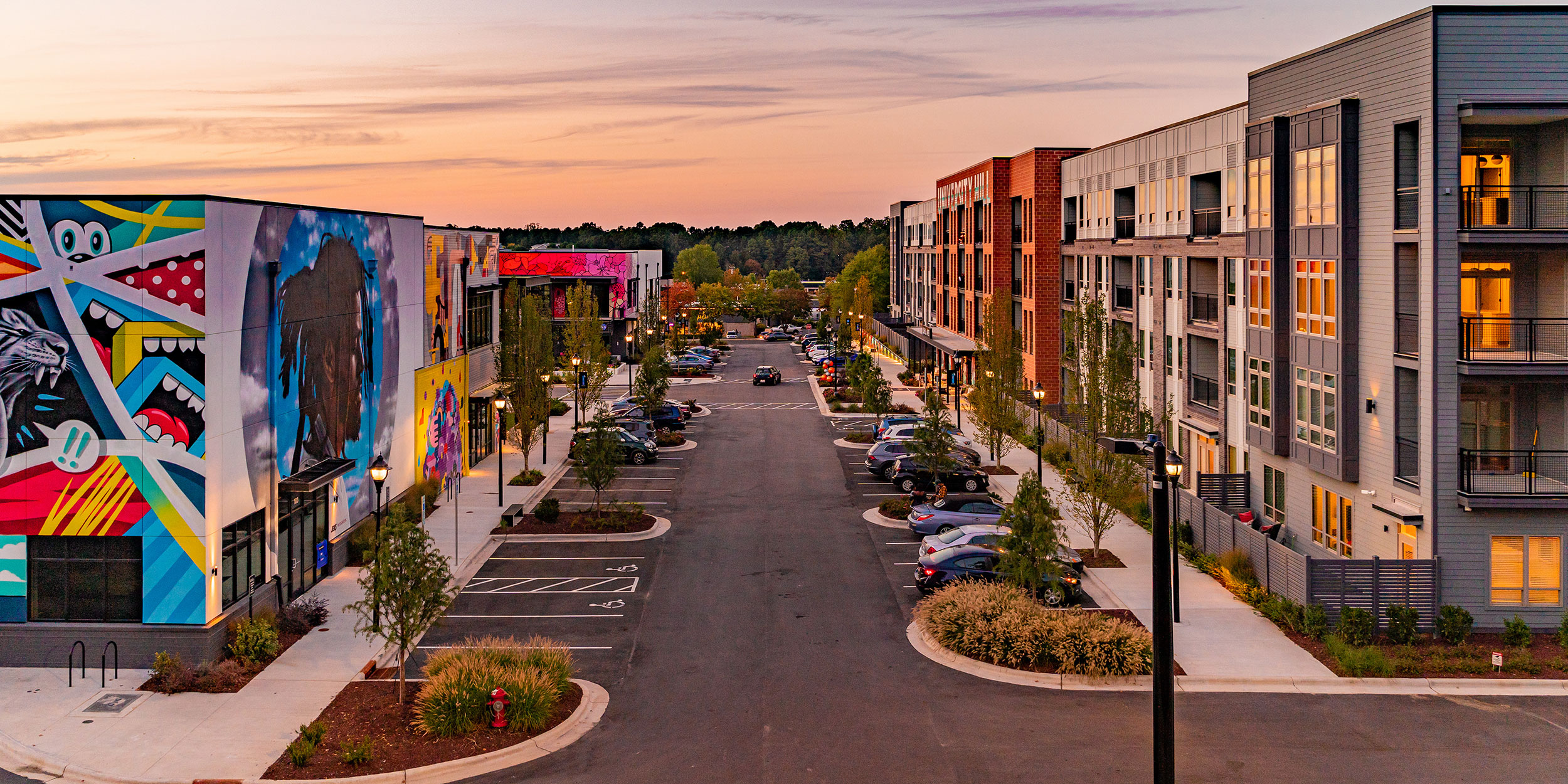Modern apartment building across from large colorful wall murals during sunset in University Hill in Wake County