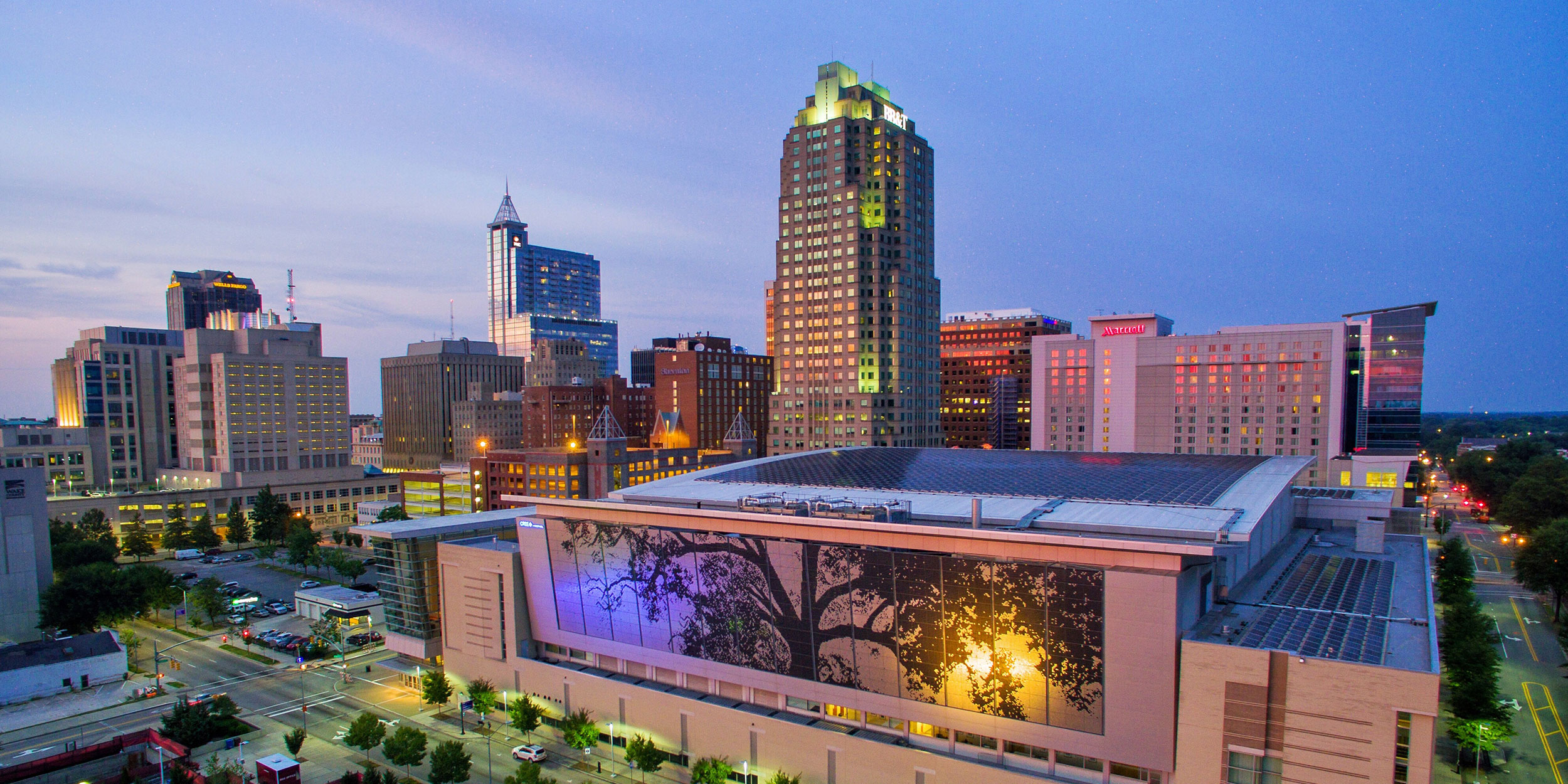 An aerial view of downtown with a convention center and skyscrapers at dusk in Wake County