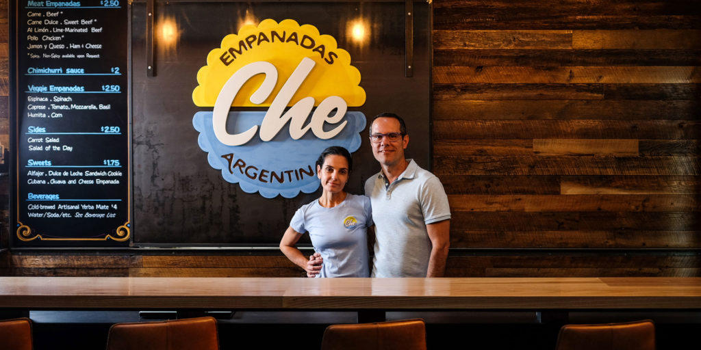 A couple stand proudly in front of a menu for their restaurant that offers cuisine from Argentina in Wake County