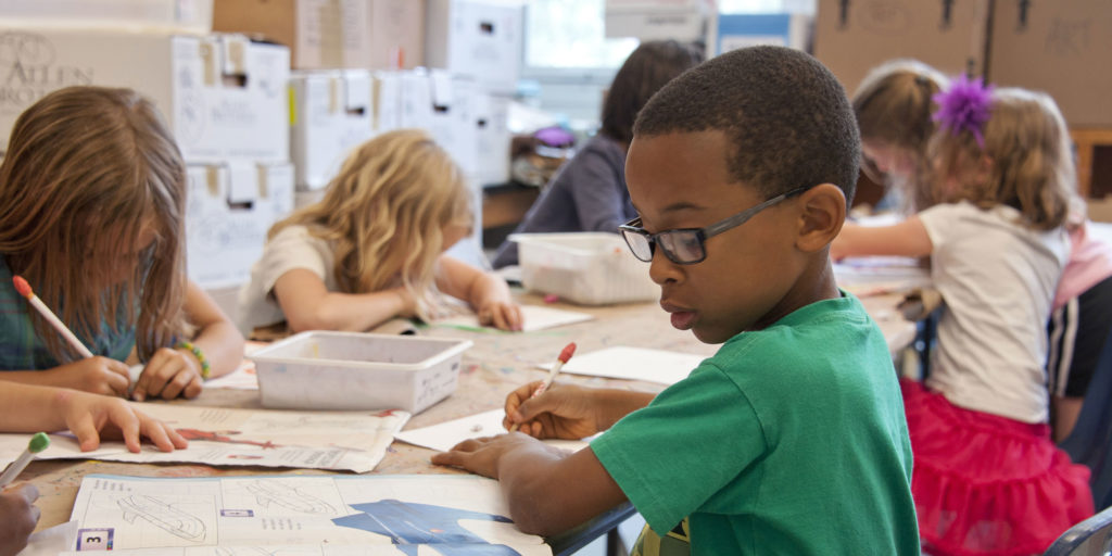 A young boy in a green shirt is following a drawing book with other students at the table in Wake County