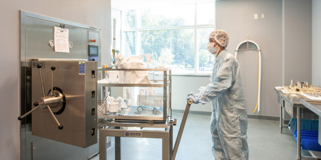 An employee of a laboratory wearing head to toe protective gear and a face mask wheeling materials into a vault in Wake County