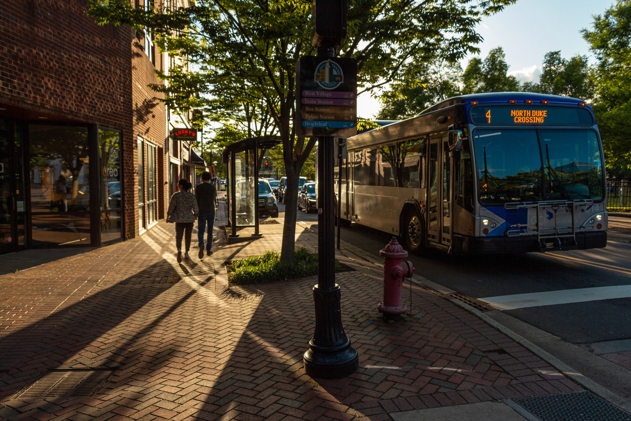 A bus stop in Durham at midday with brick buildings and a sign with local attractions in Wake County