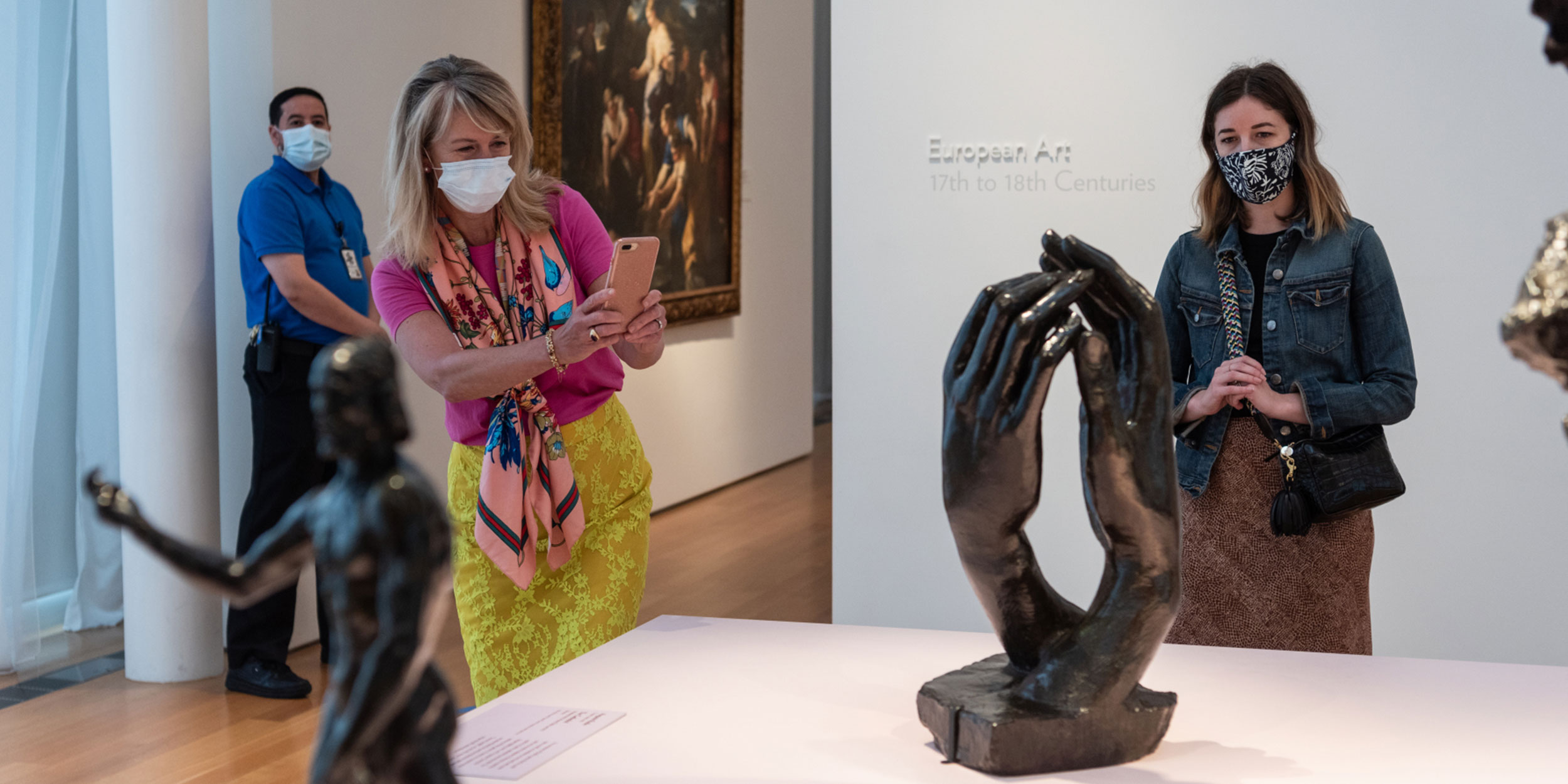 A woman in vibrant clothing takes a picture of a sculpture of two hands intertwining at a museum in Wake County