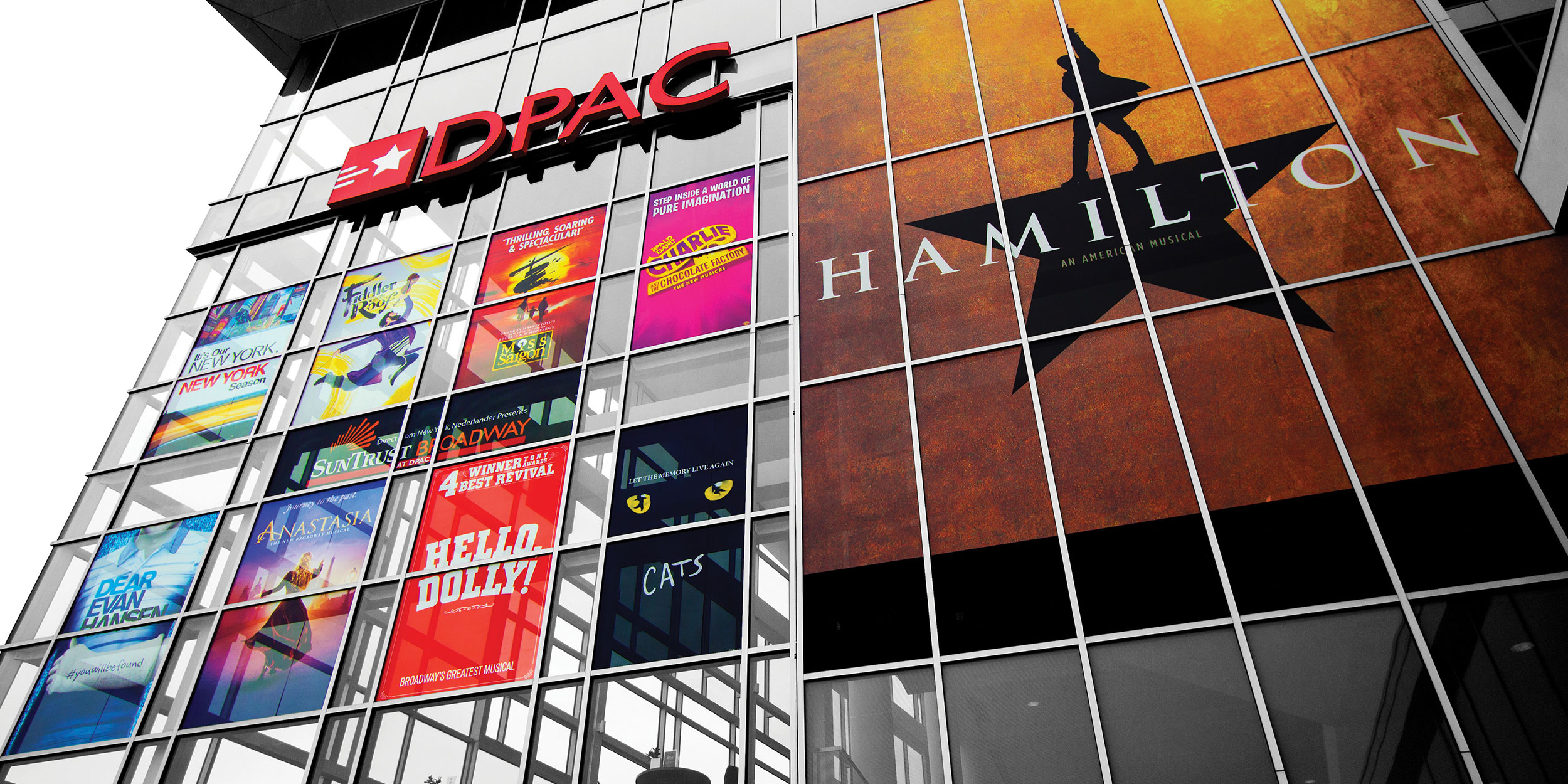 A below angle of DPAC, Durham Performing Arts Center, with different musical posters such as Cats, Hello Dolly, and Anastasia in Wake County