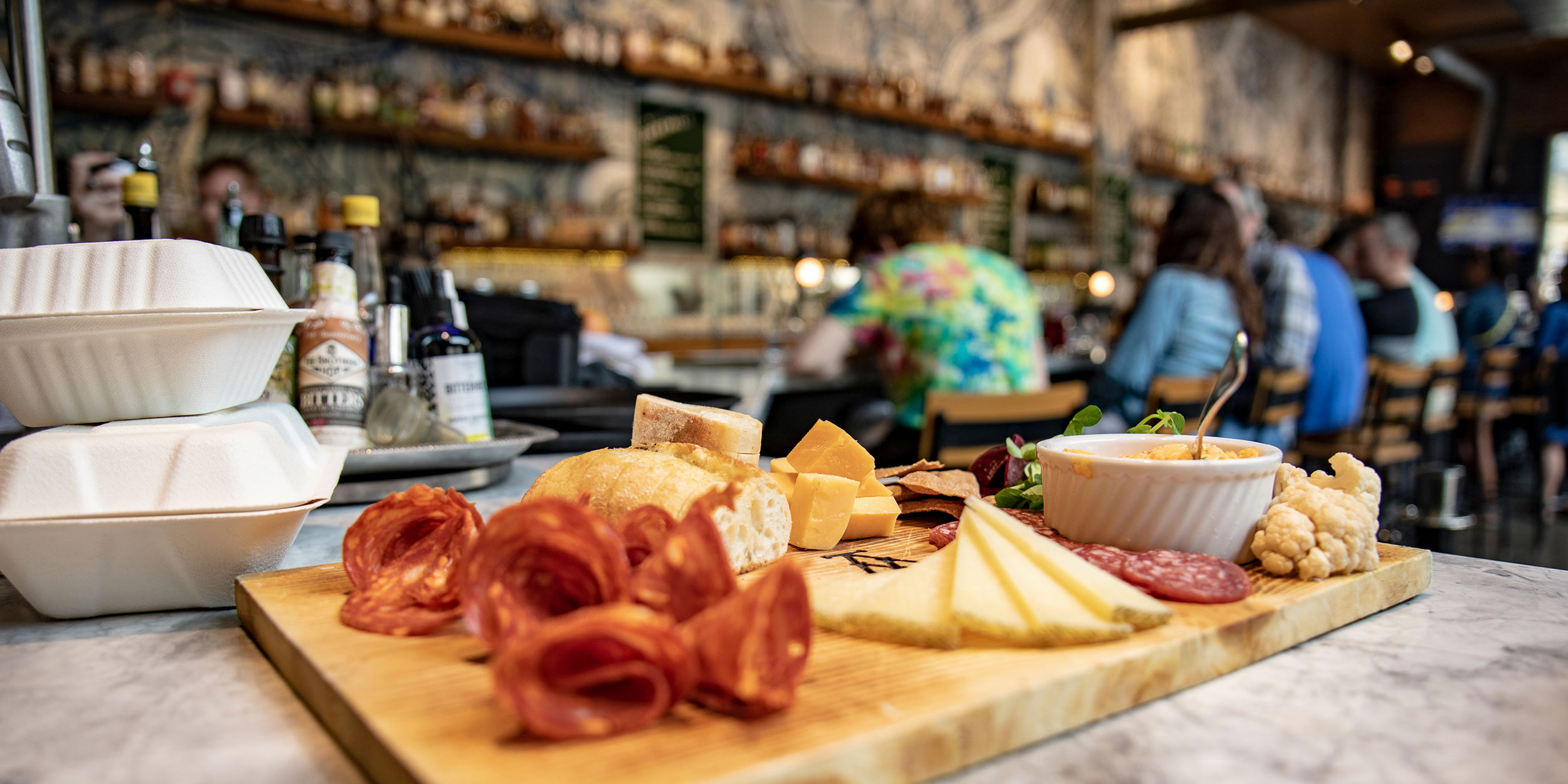 A charcuterie board filled with slices of various meats, cheeses, and fruits sits appetizingly in front of a blurred out bar in Wake County