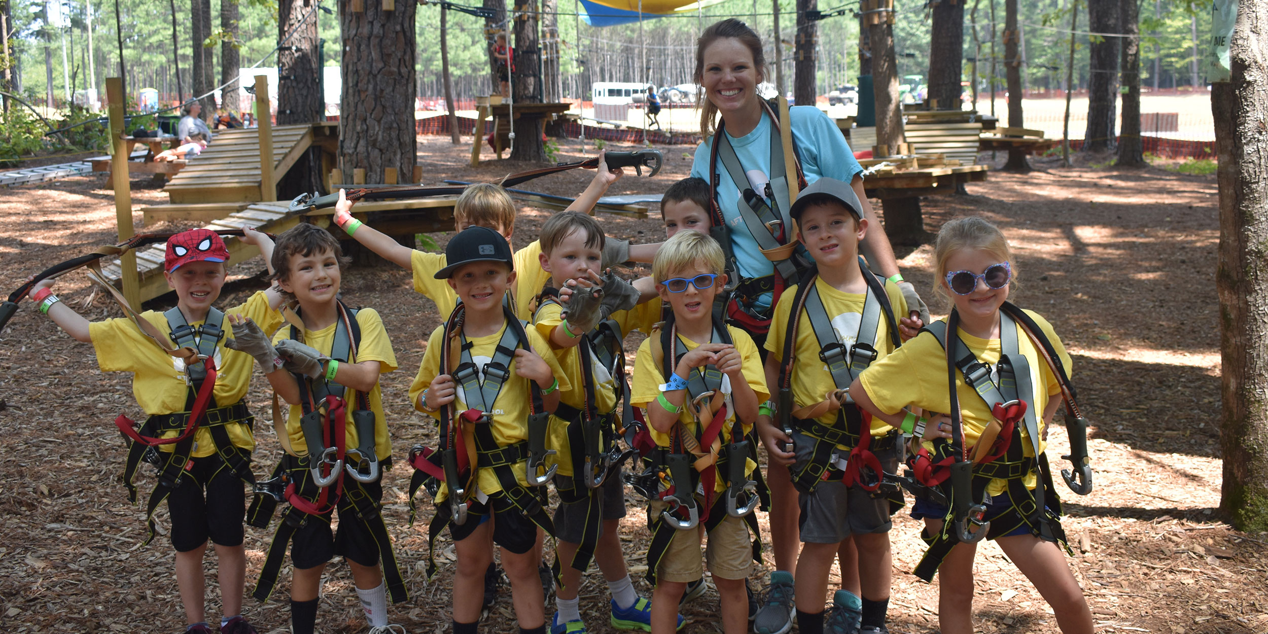 Group of young children in climbing gear with an instructor at an outdoor rock climbing and tree park in Wake County