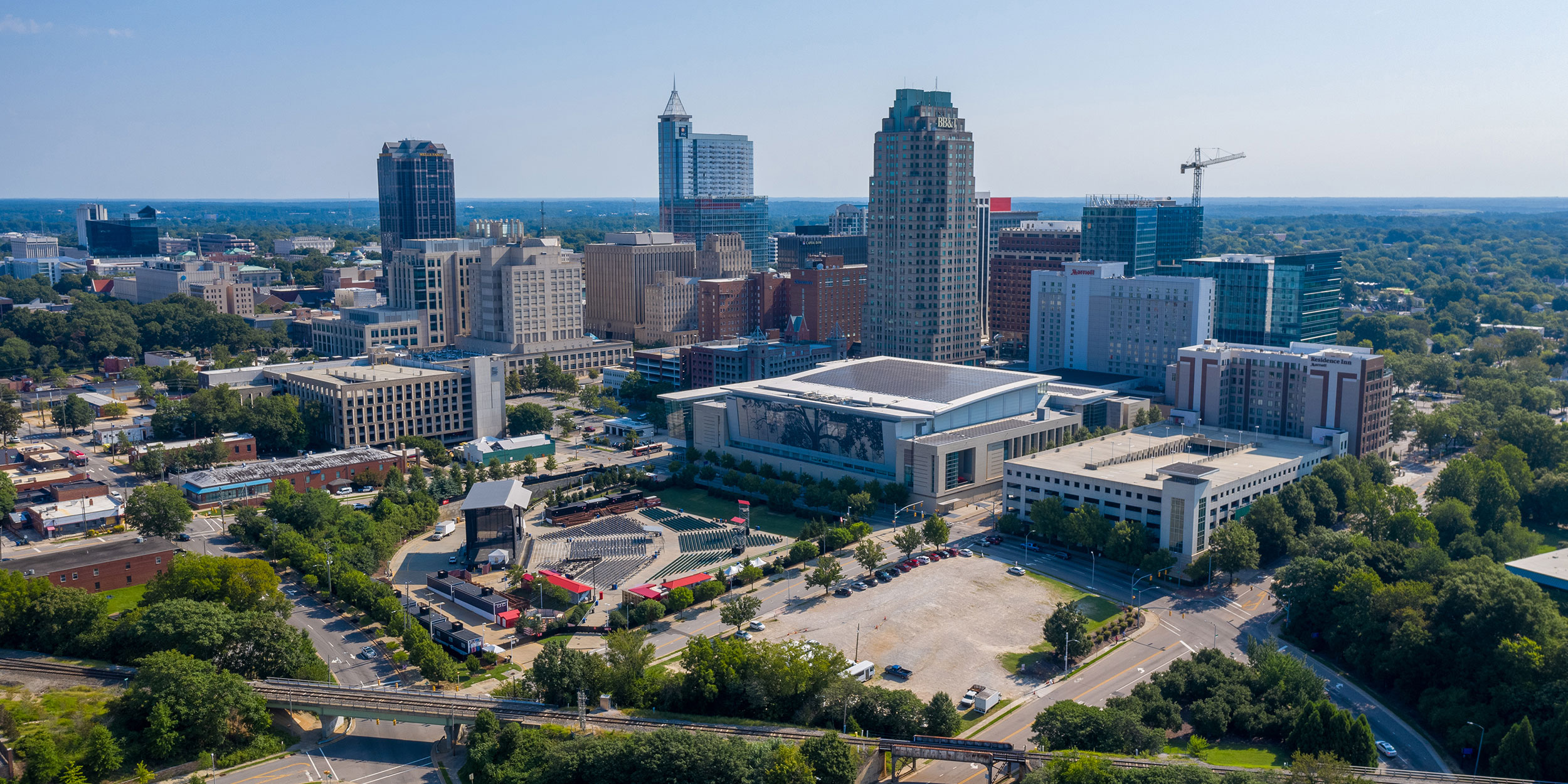 The Raleigh skyline at daytime with a view of an outdoor concert venue, the convention center, and a few skyscrapers in Wake County