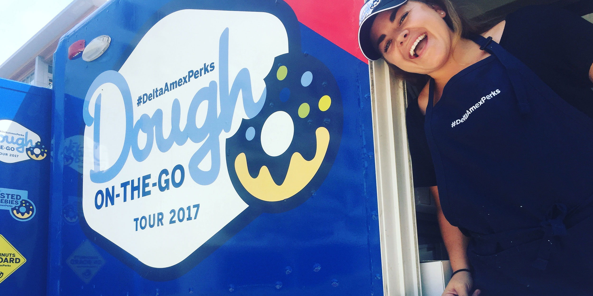 A smiling female employee leaning out the window of a Dough on the Go Foodtruck in Wake County
