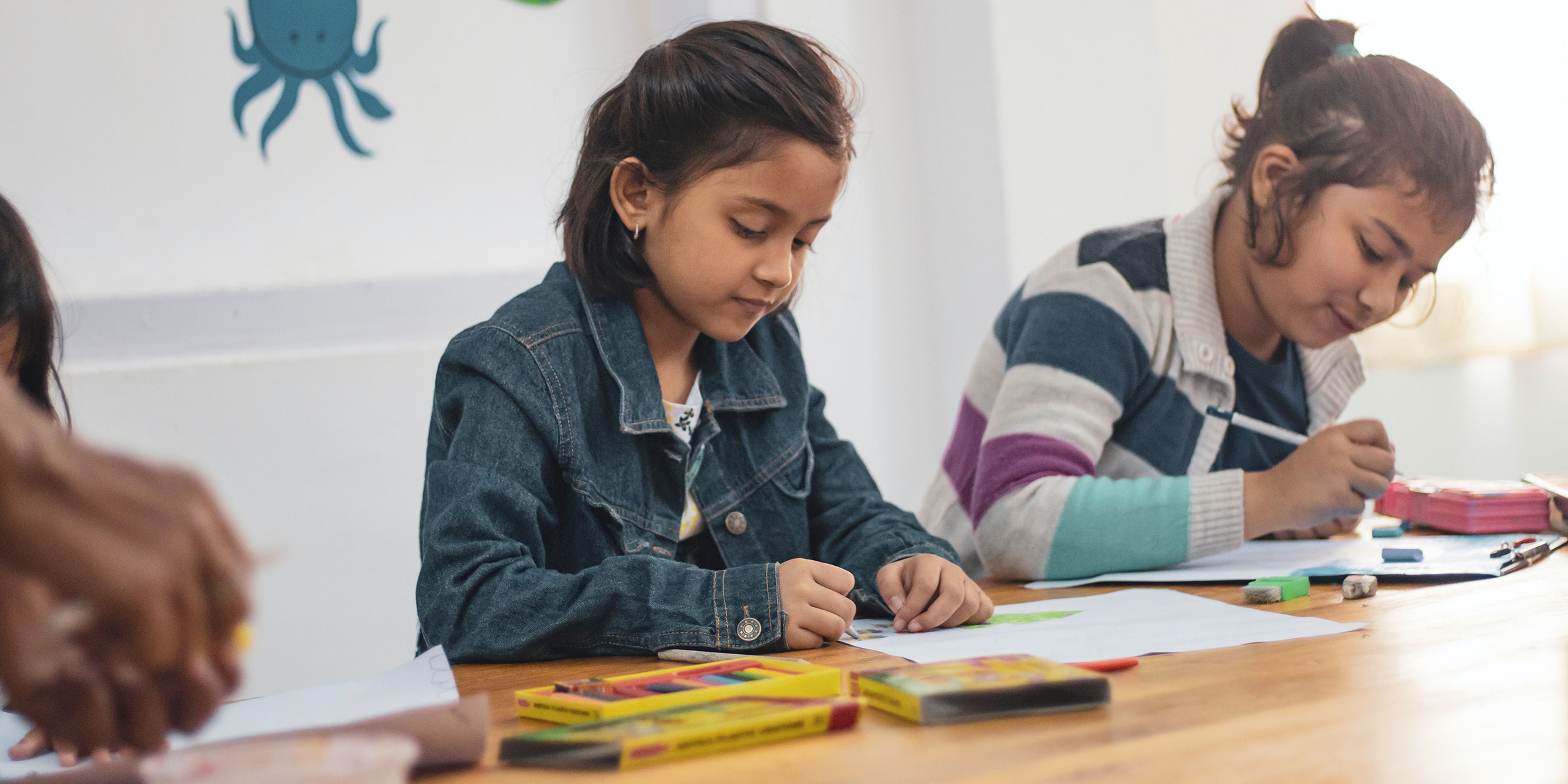 A young girl in a classroom draws a picture