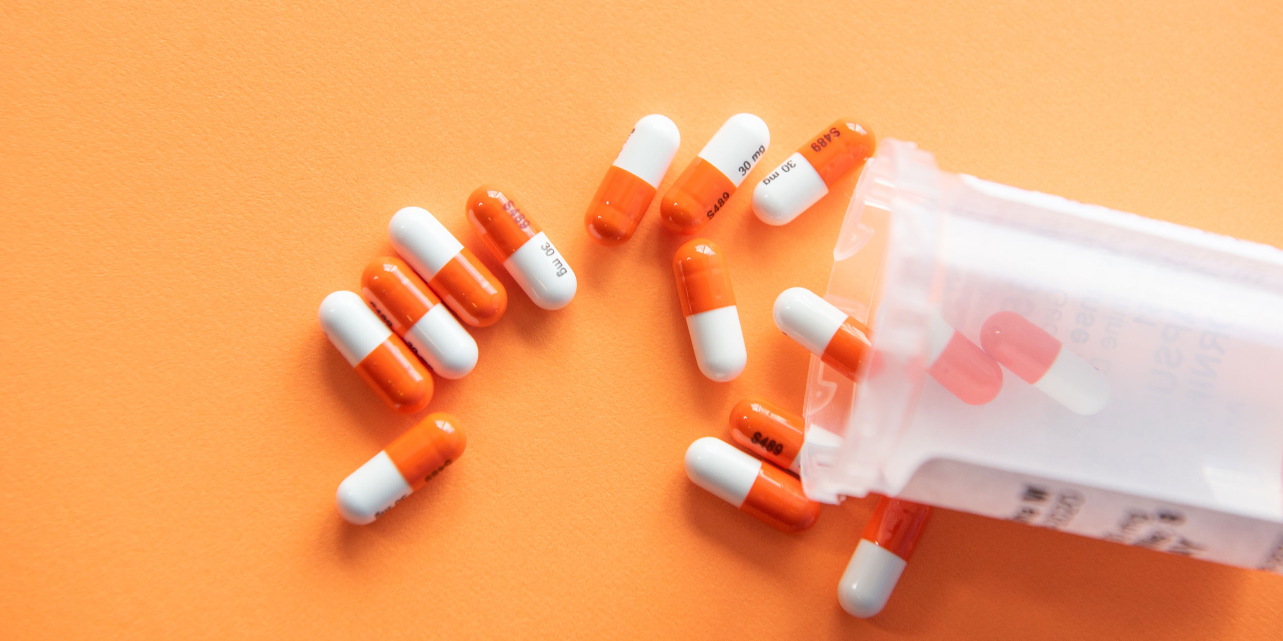 Pills coming out of a bottle onto an orange background