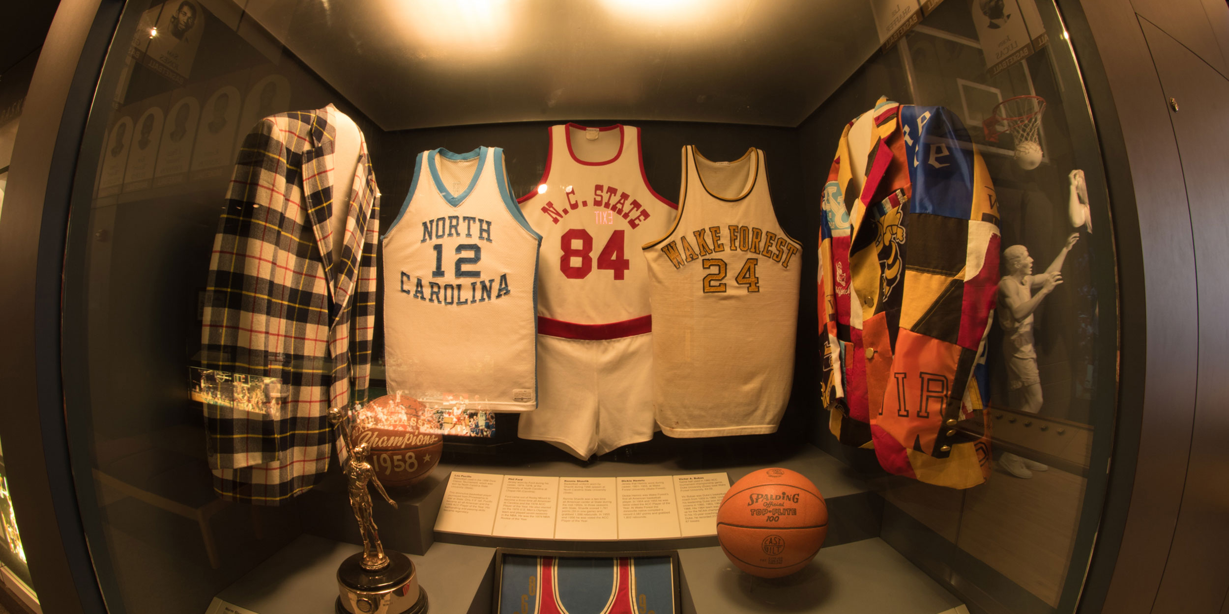 Three basketball jerseys from left to right of North Carolina, North Carolina State, and Wake Forest are on display in a museum case in Wake County