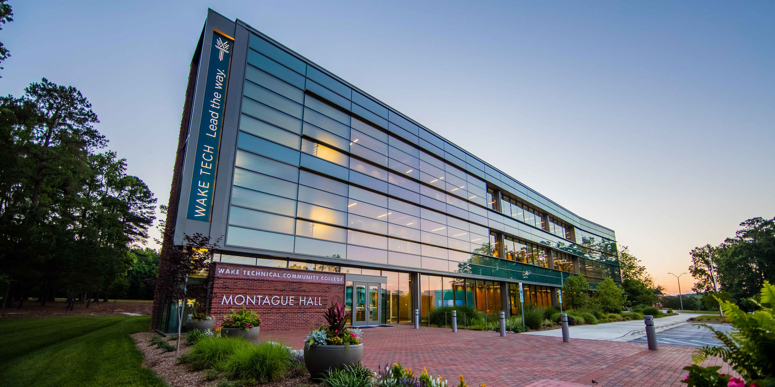 A glass building at dusk at Wake Tech with lush landscaping and a brick sign that says Montague Hall in Wake County