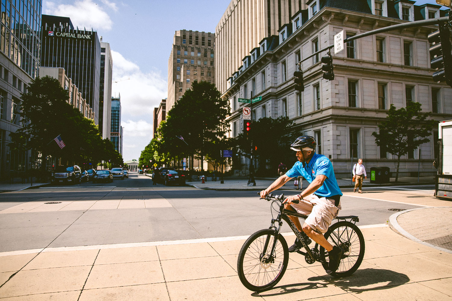 man in blue shirt riding bike on the sidewalk